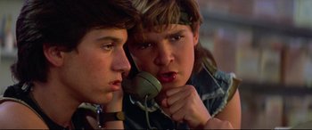 Movie still from “The Lost Boys” (1987), directed by Joel Schumacher – Two young men are looking at each other while one of them is holding a phone up to his ear; Close Up shot, Low angle