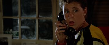 Movie still from “The Lost Boys” (1987), directed by Joel Schumacher – A young man talking on a phone in front of a window; Close Up shot, Low angle