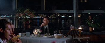 Movie still from “The Lost Boys” (1987), directed by Joel Schumacher – A man sitting at a dinner table eating a sandwich; Medium shot, Over the shoulder angle