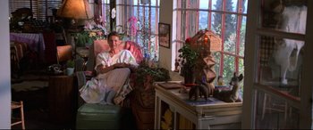 Movie still from “The Lost Boys” (1987), directed by Joel Schumacher – A woman sitting on a chair in a living room; Wide shot, High angle