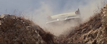 Movie still from “The Lost Boys” (1987), directed by Joel Schumacher – An old white car driving down a dirt road; Extreme Wide shot, Low angle