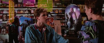 Movie still from “The Lost Boys” (1987), directed by Joel Schumacher – A man sitting in front of a display of dvds; Medium shot, Over the shoulder angle
