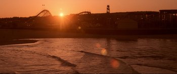 Movie still from “The Lost Boys” (1987), directed by Joel Schumacher – The sun is setting over the water with a roller coaster in the background; Extreme Wide shot, High angle