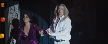 Movie still from “The Lost City” (2022), directed by Aaron Nee – A man with long blond hair and a white shirt; Medium shot, Over the shoulder angle