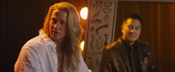 Movie still from “The Lost City” (2022), directed by Aaron Nee – A man with long blonde hair sitting next to another man with long blond hair; Medium shot, Over the shoulder angle