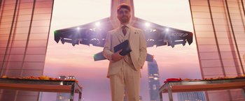 Movie still from “The Lost City” (2022), directed by Aaron Nee – A man standing in front of an airplane holding a book; Wide shot, Low angle