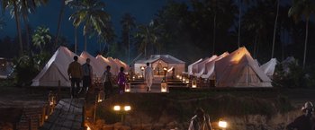 Movie still from “The Lost City” (2022), directed by Aaron Nee – A group of people walking in front of tents at night; Extreme Wide shot, High angle