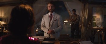 Movie still from “The Lost City” (2022), directed by Aaron Nee – A man in a white suit standing in front of a table; Medium shot, Over the shoulder angle