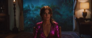 Movie still from “The Lost City” (2022), directed by Aaron Nee – A woman in a purple dress sitting in a chair; Medium shot, High angle