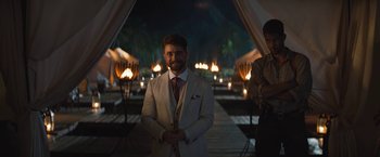 Movie still from “The Lost City” (2022), directed by Aaron Nee – A man in a white suit standing in front of candles; Wide shot, Over the shoulder angle