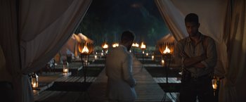 Movie still from “The Lost City” (2022), directed by Aaron Nee – A man in a white suit standing in front of candles; Wide shot, Over the shoulder angle