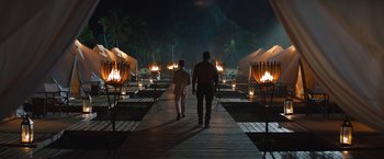 Movie still from “The Lost City” (2022), directed by Aaron Nee – Two people walking down a wooden walkway at night; Wide shot, Over the shoulder angle