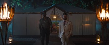 Movie still from “The Lost City” (2022), directed by Aaron Nee – Two men standing in front of a tent at night; Wide shot, Over the shoulder angle