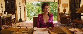 Movie still from “The Lost City” (2022), directed by Aaron Nee – A woman sitting at a table in front of papers; Medium shot, Over the shoulder angle