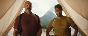 Movie still from “The Lost City” (2022), directed by Aaron Nee – Two men standing next to each other in front of a mountain; Medium shot, Low angle