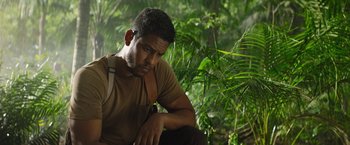 Movie still from “The Lost City” (2022), directed by Aaron Nee – A man sitting in the woods with his hand on his shoulder; Close Up shot, Low angle