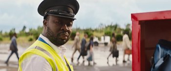 Movie still from “The Lost City” (2022), directed by Aaron Nee – A man wearing a yellow vest and a black hat; Close Up shot, Over the shoulder angle