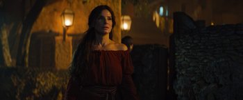 Movie still from “The Lost City” (2022), directed by Aaron Nee – A woman in a red dress standing next to a wall; Medium shot, Over the shoulder angle