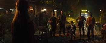 Movie still from “The Lost City” (2022), directed by Aaron Nee – A group of men standing in a courtyard at night; Wide shot, Over the shoulder angle