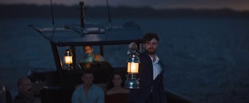 Movie still from “The Lost City” (2022), directed by Aaron Nee – A man holding a lantern while standing on a boat in the ocean; Wide shot, Over the shoulder angle