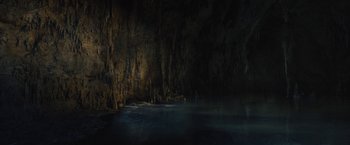Movie still from “The Lost City” (2022), directed by Aaron Nee – A painting of a dark cave with a body of water in the foreground; Extreme Wide shot, High angle