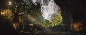 Movie still from “The Lost City” (2022), directed by Aaron Nee – A view of a waterfall from the side of a bridge; Extreme Wide shot, Low angle