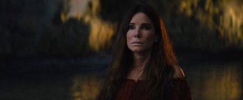 Movie still from “The Lost City” (2022), directed by Aaron Nee – A beautiful woman with long brown hair standing next to a body of water; Close Up shot, Over the shoulder angle
