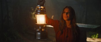 Movie still from “The Lost City” (2022), directed by Aaron Nee – A woman holding a lantern in a dark room; Medium shot, Low angle