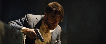 Movie still from “The Lost City” (2022), directed by Aaron Nee – A man in a suit and tie holding a gun in his hand; Close Up shot, High angle