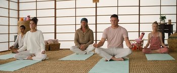 Movie still from “The Lost City” (2022), directed by Aaron Nee – Two men sitting on the ground doing yoga; Wide shot, Low angle