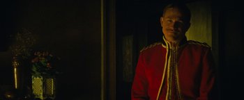 Movie still from “The Lost City of Z” (2016), directed by James Gray – A man in a red and gold uniform standing next to a wall; Medium shot, Over the shoulder angle