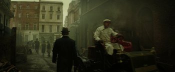 Movie still from “The Lost City of Z” (2016), directed by James Gray – A man in a suit and hat is walking down the street with another man; Wide shot, Over the shoulder angle