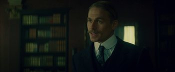 Movie still from “The Lost City of Z” (2016), directed by James Gray – A man in a suit and tie in front of a book case; Close Up shot, Over the shoulder angle