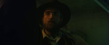 Movie still from “The Lost City of Z” (2016), directed by James Gray – A man with a beard wearing glasses and a hat; Close Up shot, Over the shoulder angle