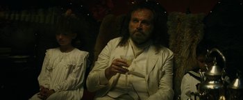 Movie still from “The Lost City of Z” (2016), directed by James Gray – A man with long hair and a beard holding a glass of wine; Medium shot, Over the shoulder angle