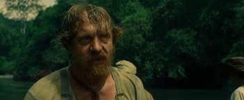 Movie still from “The Lost City of Z” (2016), directed by James Gray – A man with long hair and a goatee is standing outside; Close Up shot, Over the shoulder angle