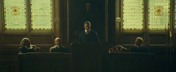 Movie still from “The Lost City of Z” (2016), directed by James Gray – A man standing at the top of a podium in front of two other men; Wide shot, Low angle
