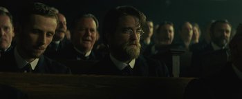 Movie still from “The Lost City of Z” (2016), directed by James Gray – A man with a long beard and glasses in a dark room; Medium shot, Over the shoulder angle