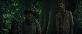 Movie still from “The Lost City of Z” (2016), directed by James Gray – A man with a beard wearing a hat standing next to a tree; Medium shot, Low angle