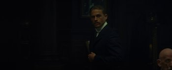 Movie still from “The Lost City of Z” (2016), directed by James Gray – A man wearing a suit and tie in a dark room; Medium shot, Over the shoulder angle