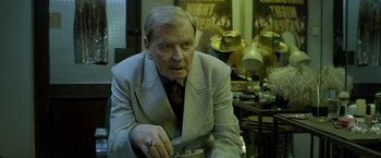 Movie still from “The Lure” (2015), directed by Agnieszka Smoczynska – An older man wearing a suit and tie holding a camera; Close Up shot, Over the shoulder angle