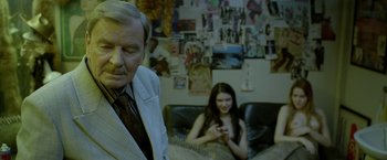 Movie still from “The Lure” (2015), directed by Agnieszka Smoczynska – An older man and a young woman sitting on a couch in a room; Medium shot, Over the shoulder angle
