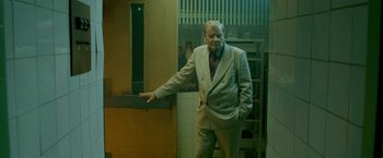 Movie still from “The Lure” (2015), directed by Agnieszka Smoczynska – An older man wearing a suit and tie standing next to a door; Medium shot, Over the shoulder angle