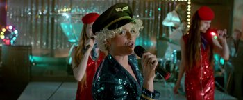 Movie still from “The Lure” (2015), directed by Agnieszka Smoczynska – A woman in a hat is singing into a microphone; Medium shot, Low angle