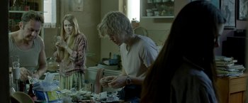 Movie still from “The Lure” (2015), directed by Agnieszka Smoczynska – A man in a white t - shirt is looking down at a stack of papers; Medium shot, Over the shoulder angle