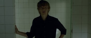Movie still from “The Lure” (2015), directed by Agnieszka Smoczynska – A man in a black shirt standing in front of a tiled wall; Medium shot, Low angle