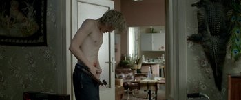 Movie still from “The Lure” (2015), directed by Agnieszka Smoczynska – A shirtless man holding a knife in a kitchen; Medium shot, Over the shoulder angle