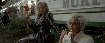 Movie still from “The Lure” (2015), directed by Agnieszka Smoczynska – Two women are sitting on a bench and one of them is smoking a cigarette; Medium shot, Low angle