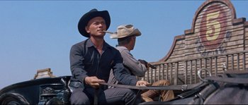 Movie still from “The Magnificent Seven” (1960), directed by John Sturges – Two men in cowboy hats sitting on a bench; Medium shot, Low angle
