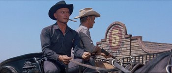 Movie still from “The Magnificent Seven” (1960), directed by John Sturges – Two men in cowboy hats are riding a horse and smoking a cigar; Medium shot, Low angle